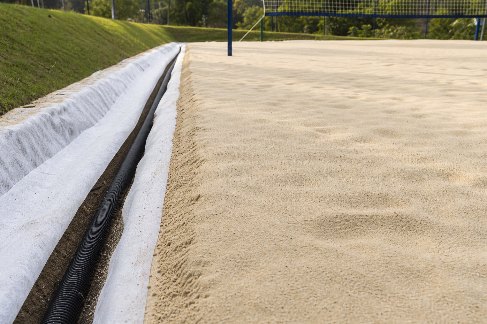 Quadra residencial de beach tennis mostrando areia lisa e sistema de drenagem em espinha de peixe.