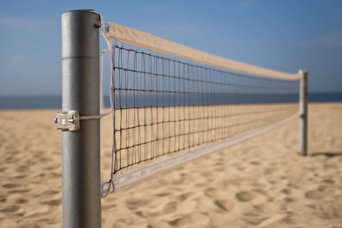 Postes de aço galvanizado com rede esticada em quadra de beach tennis na areia.
