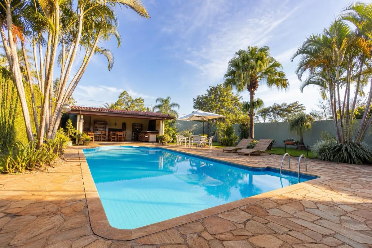 Piscina ampla com deck de pedra ao sol da manhã, coqueiros ao fundo, espaço perfeito para almoço familiar.